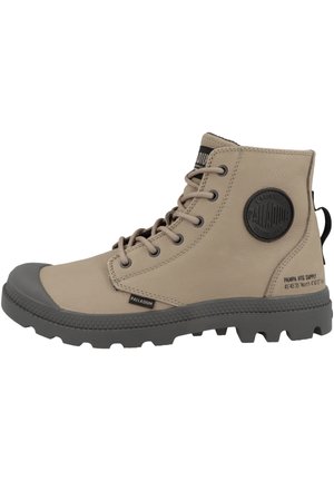 Stivali alla caviglia in pelle beige con punta e suola in gomma grigia. Presentano lacci spessi, dettagli testurizzati e una patch rotonda con il logo sul lato.