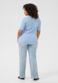 Top de manga corta de color azul claro con textura de canalé, combinado con pantalones rectos de denim azul claro. El top tiene un dobladillo curvado y un ajuste relajado. Zapatos planos negros.