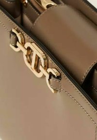 Borsa a mano in pelle marrone con dettagli in oro, caratterizzata da una chiusura con logo prominente e scomparti interni per l'organizzazione. Texture liscia.