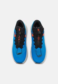 Baskets de sport bleues en maille et matériau synthétique, avec une doublure intérieure noire, des lacets élastiques et des accents orange.