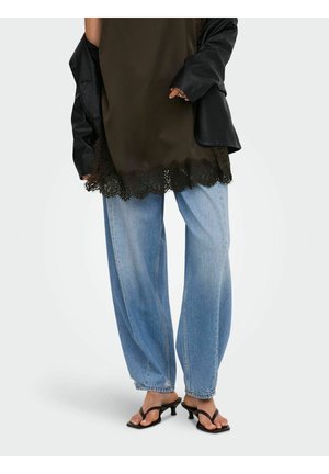 Personne portant un jean bleu clair à jambes larges, des sandales à talons noires, un haut vert olive avec bordure en dentelle noire et une veste noire posée.
