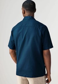 Camicia a maniche corte con bottoni in tessuto blu navy scuro, caratterizzata da un'orlo dritto, yoke posteriore e texture morbida.