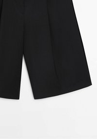 Musta räätälöity shortsit, joissa löysä istuvuus ja terävät taitokset. Valmistettu kudotusta kankaasta, sivutaskuilla ja siistillä, minimalistisella muotoilulla.