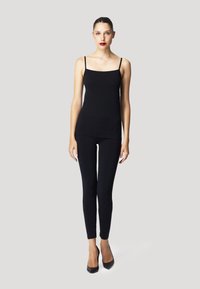 Svart linne med tunna band, parat med svarta leggings. Modellen bär svarta spetsiga klackar, mot en simpel bakgrund. Slät textur, minimalistisk design.