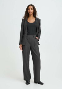 Grå skræddersyet jakkesæt med lange, lige bukser og en tætsiddende blazer, parret med en sort tanktop. Glat stof med subtil tekstur.