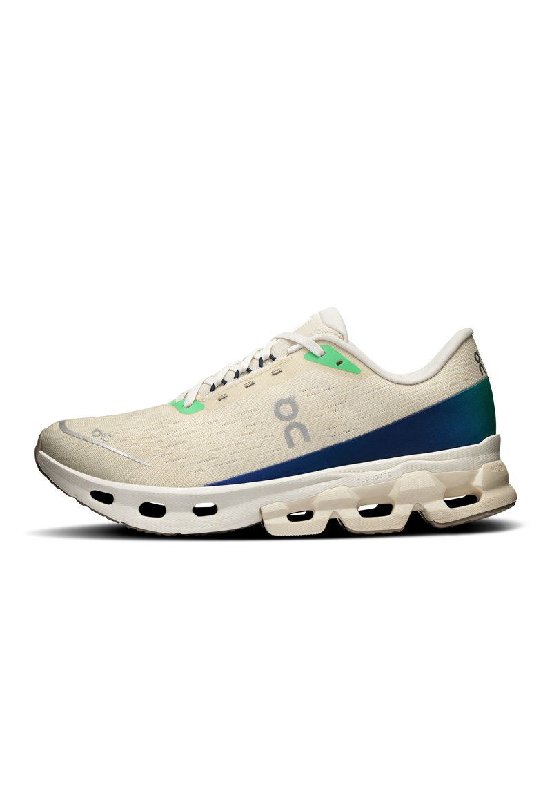 Light beige athletic shoe with green and navy accents. Features a textured mesh upper, flat laces, and a cushioned sole with cut-outs.