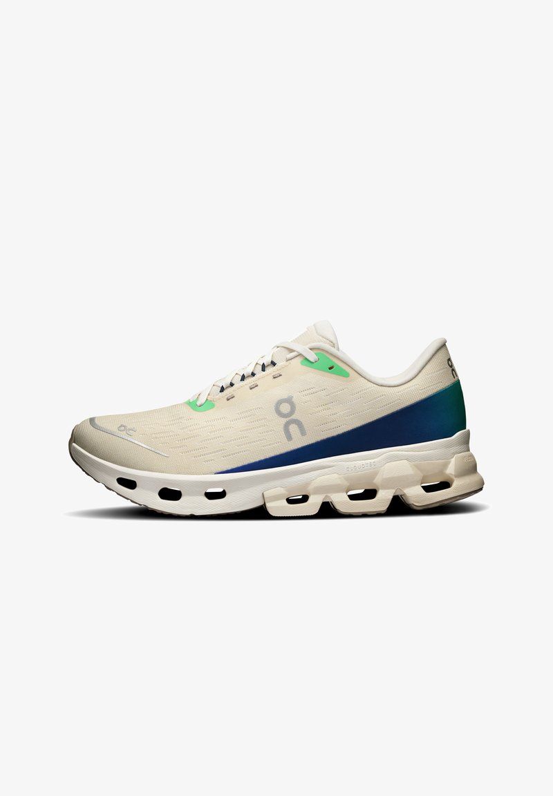 Light beige athletic shoe with green and navy accents. Features a textured mesh upper, flat laces, and a cushioned sole with cut-outs.