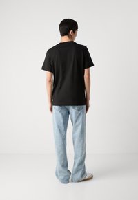 Black cotton t-shirt with short sleeves, paired with light blue denim flared jeans and white sneakers. Plain rear view, minimal details.