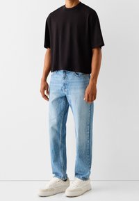 Czarny skrócony T-shirt, krótkie rękawy, okrągły dekolt. Jasnoniebieskie dżinsy, prosty krój, z wyblakł ą fakturą. Białe sneakersy, płaskie, z teksturowaną podeszwą.