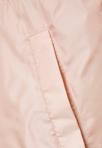 Vaaleanpunainen kangas, jossa on sileä pinta, sisältää piilotetun taskusauman, joka näyttää hienon ompelun ja ruutukuosin materiaalissa.