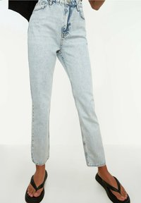 Ljusblå denimjeans med hög midja, raka ben och fransad fåll. Kombineras med svarta flip-flops med en tunn remdesign.