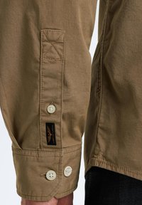 Khaki shirt met mouwen die zijn voorzien van een knoopmanchet met twee knopen, gestikte details en een geweven label. Gladde stof met een matte afwerking.
