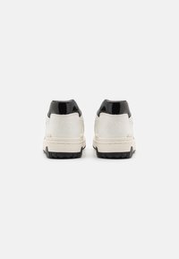 Vita lädersneakers med svart lackklack, texturerade detaljer och gummisula. Innehåller präglad logotyp och minimala sömdetaljer.