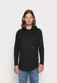 Sort langærmet hættetrøje med en afslappet pasform, der har snøre i hætten og en glat tekstur. Bæres med blå jeans.