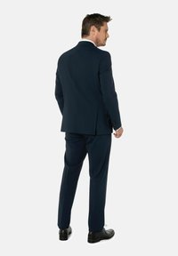 Marineblauer Anzug mit modernem Schnitt, einer Schlitzöffnung hinten und passender Hose. Abgerundet mit schwarzen Schnürschuhen und einem weißen Kragenakzent.