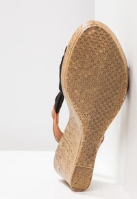 Chaussure en tissu noir avec un talon en liège, dotée d'une semelle en caoutchouc texturée avec un motif à carreaux. Étiquette de taille 37 visible sur la semelle.