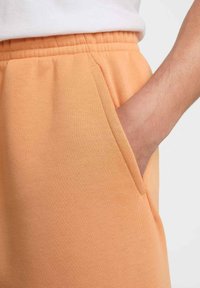 Pantalones de chándal de color melocotón fabricados con una mezcla de algodón, con una textura suave, cinturilla elástica y bolsillos laterales.