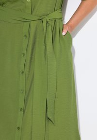 Abito verde realizzato in tessuto leggero, con una chiusura a bottoni sul davanti, una cintura legata in vita e una finitura testurizzata, completa di tasche laterali.