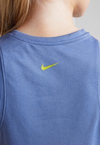 Niebieska bezrękawnikowa bluzka wykonana z gładkiego materiału, z małym żółtym logo Nike z tyłu, okrągłym dekoltem i przeszytymi szwami.
