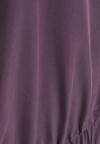 Fialová látka s hladkou texturou, s jemným řasením a sbíráním detailů na spodní části. Bez viditelných vzorů nebo kovových součástí.