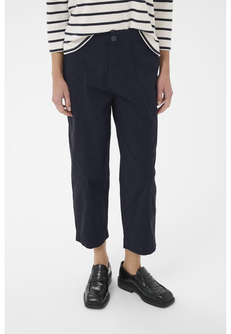 Pantalons cropped bleu marine en coton, avec une fermeture à boutons à l'avant, des poches latérales et une coupe décontractée. Associés à des mocassins noirs.