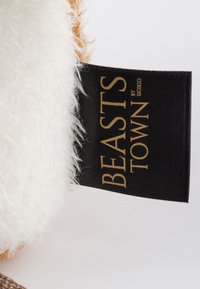 Peluche avec une douce fourrure blanche et des accents marron. Présente une étiquette noire avec "BEASTS TOWN" en lettres dorées, indiquant la marque.