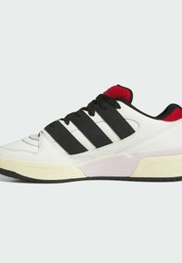 White leather sneaker with black stripes, red mesh accents, and a thick rubber sole. Features black laces and a textured surface.