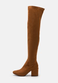 Botas marrones de ante hasta la rodilla con punta en forma de flecha y tacón ancho, que presentan una textura suave y un diseño ajustado.