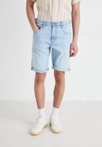 Șorturi din denim de un albastru deschis, cu manșete răsucite, cinci buzunare și închidere cu nasture, asortate cu adidași albi și șosete albe cu model de rețea.