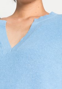 Maglione azzurro chiaro in maglia con scollatura a V, caratterizzato da dettagli a coste e una texture morbida. Il tessuto sembra leggero e traspirante.