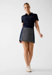 Polo bleu marine associé à une jupe à motifs géométriques dans des nuances de bleu marine et blanc. Des baskets blanches complètent le look.