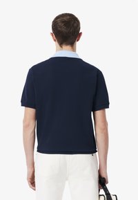 Marinblå polo skjorta med ljusblå krage, korta ärmar och en slät textur. Har en rak passform och ribbade ärmslut.