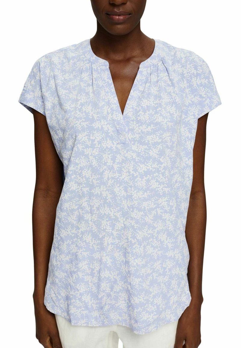 Blusa floreale azzurro chiaro con maniche corte, scollatura a V, tessuto morbido, sottile motivo floreale bianco e vestibilità ampia per il comfort.