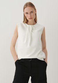 Weiße ärmellose Bluse mit einer Drapierung am Ausschnitt, kombiniert mit schwarzen Hosen. Glatter Stoff, minimalistisches Design.