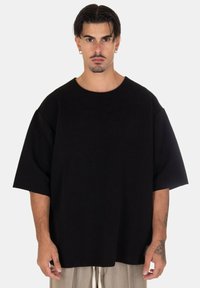 T-shirt nera oversize con un motivo testurizzato a coste. Collo tondo, maniche corte, abbinata a pantaloni chiari a vestibilità rilassata.
