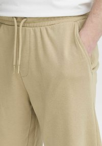 Un pantalon de survêtement beige en tissu doux avec une taille élastique, un cordon de serrage et des poches latérales. Design décontracté et confortable.