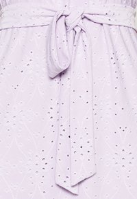 Lavender fabric with intricate eyelet design and subtle floral pattern. Features a tied belt at the waist, adding structure to the garment.