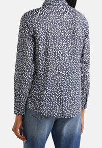 Långärmad skjorta med marinblå bakgrund och små vita och gula blommönster, med krage och avslappnad passform. Visas med jeans.