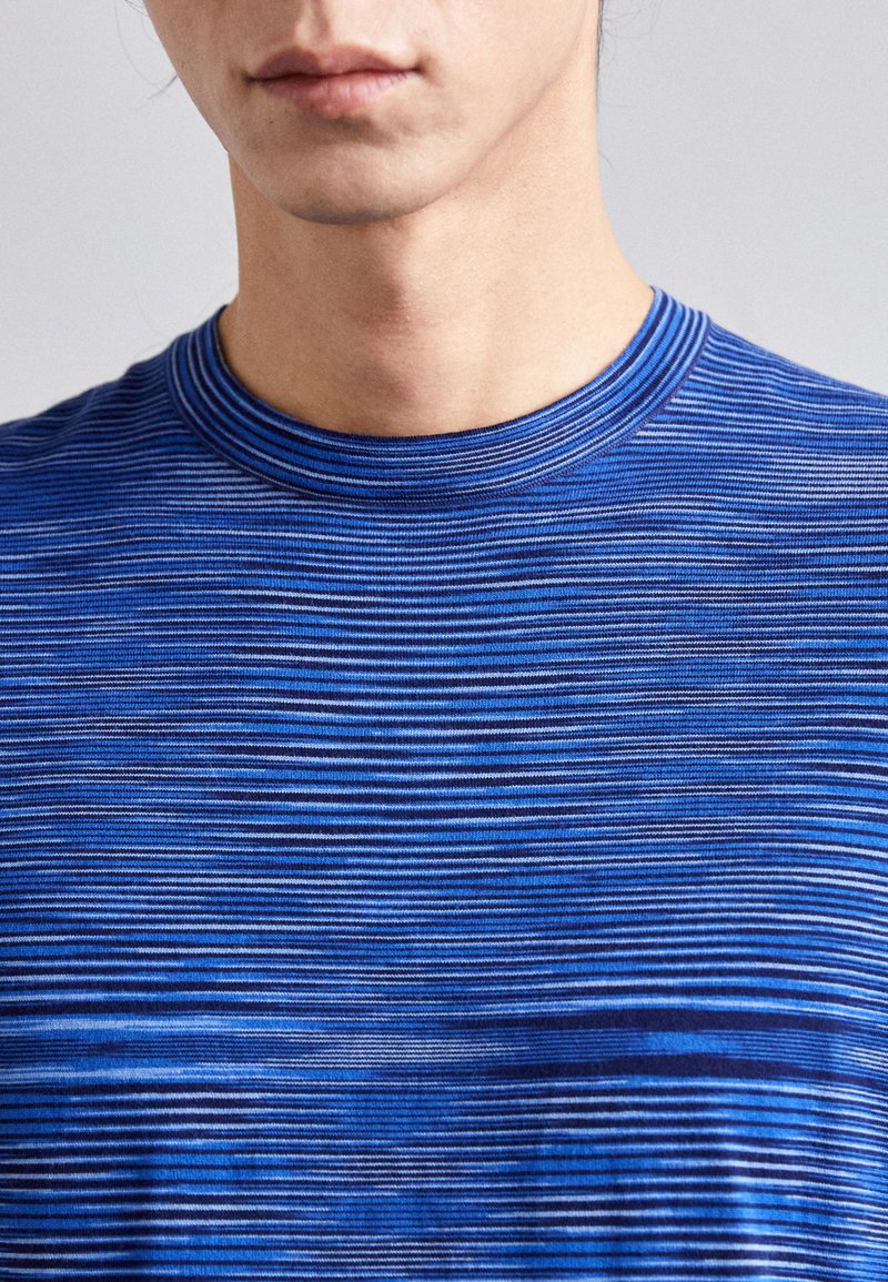 Blauwe gestreepte T-shirt met korte mouwen en een ronde halslijn. Kenmerkt zich door verschillende tinten blauw en een gladde textuur, met horizontale lijnen in de nadruk.