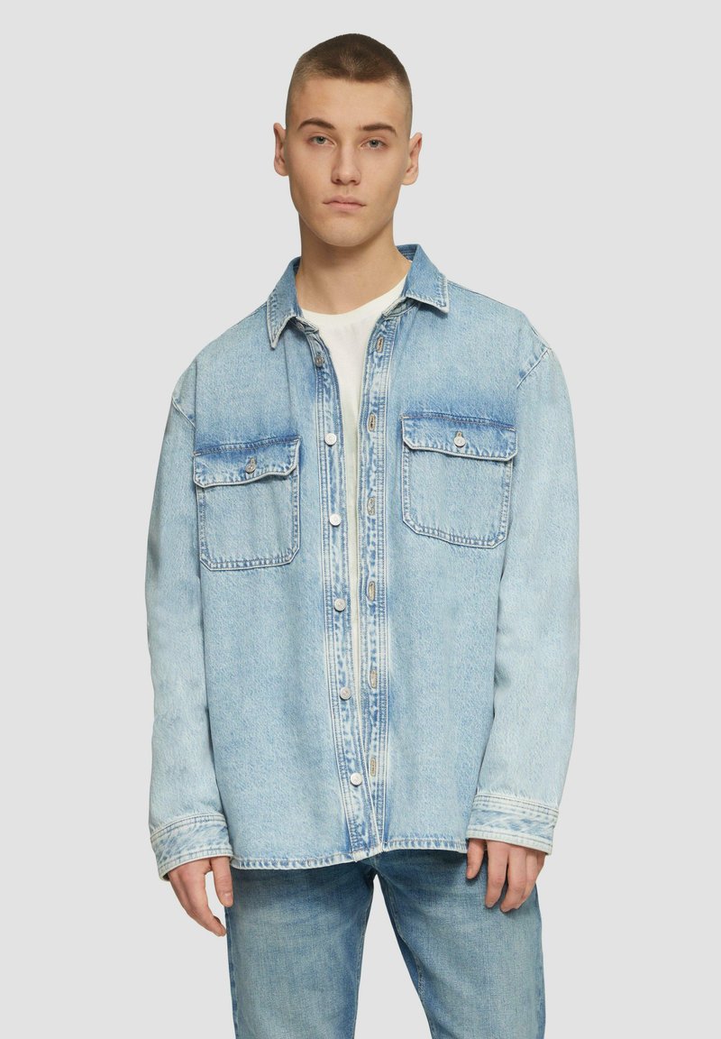 Jasnoniebieska koszula z denimu z dwoma kieszeniami na piersi, z zapięciem na guziki i luźnym krojem. Posiada widoczne szwy i lekko wyblakłą fakturę.