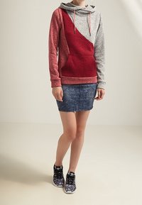 Felpa con cappuccio caratterizzata da un design a spacco di trame rosse e grigie, con tasca a marsupio. Abbinata a una gonna mini in denim e scarpe da ginnastica con motivo.