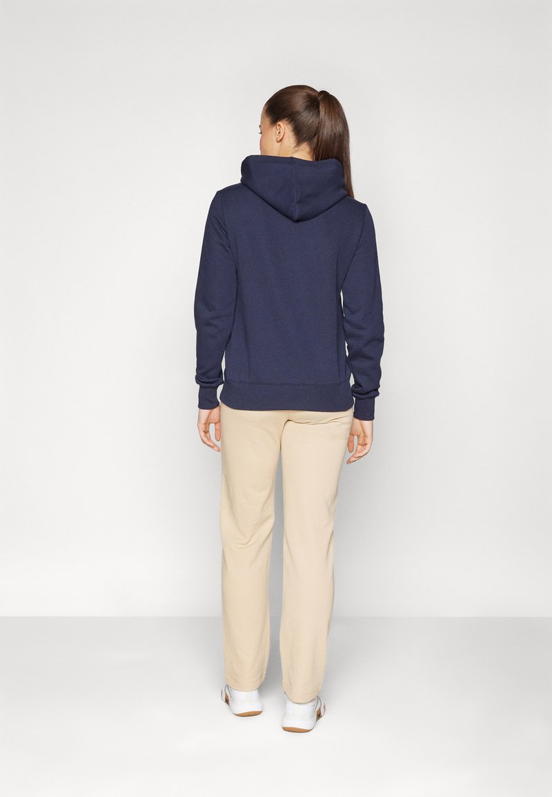 Sweat-shirt à capuche bleu marine avec une poche kangourou et des poignets côtelés, associé à un pantalon beige. Tissu doux, coupe décontractée et design simple.