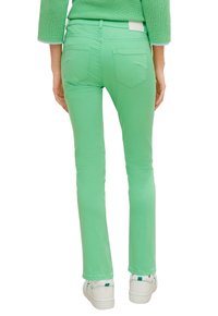 Pantalons en denim extensible vert avec une coupe slim, dotés de deux poches arrière, et associés à des baskets blanches pour un look décontracté.