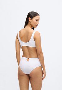 Valge bikiinikomplekt, millel on laiad rihmad ja klambri detailiga kauss-kaelusega ülaosa ning kõrge vöökohaga püksikud ümmarguse lõikega aktsendiga.