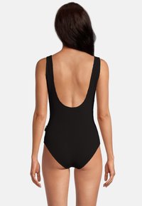 Maillot de bain une pièce noir à côtes avec un décolleté profond dans le dos, des bretelles larges et un design sans couture, offrant une apparence lisse et texturée.