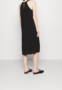 Mustat ilmanhihoiset mekko, jossa on avainrei'ellä varustettu suljenta takana, valmistettu teksturoidusta kankaasta, ulottuu keskimäärin pohkeeseen saakka. Yhdistetty yksinkertaisiin mustiin liukuviin kenkiin.