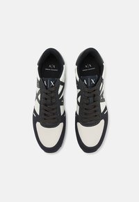 Sneakers brancos e marinho com parte superior em malha e sintético, apresentando atacadores castanho-escuros, detalhes do logótipo e um design de bico redondo.