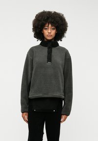 Γκρίζος φλις πουλόβερ με ψηλό γιακά και μαύρες λεπτομέρειες. Διαθέτει μπροστινό φερμουάρ, άνετη εφαρμογή και υφή υφάσματος. Μαύρο παντελόνι από κάτω.