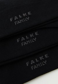 Crne čarape s natpisom "FALKE FAMILY" u sivoj boji. Materijal izgleda mekano s glatkom teksturom i jednostavnim, klasičnim dizajnom.