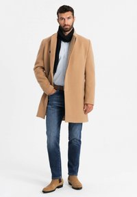Kamelhaarmantel, schwarzer Schal, gestreiftes Button-up-Hemd, blaue Jeans, beige Stiefel. Modernes Design mit klaren Linien und maßgeschneiderter Passform.